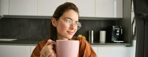 retrato do lindo morena mulher, sentado dentro cozinha, levando uma pausa para copo do café. menina bebidas chá às casa foto