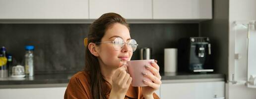 retrato do jovem mulher em repouso, tendo xícara. menina bebidas chá dentro cozinha, detém caneca e parece pensativo foto