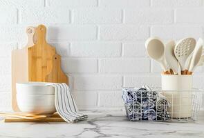 uma conjunto do cozinha utensílios em uma luz pedra bancada contra uma branco tijolo muro. cozinha têxteis. uma acolhedor cozinha com não desperdício. frente visualizar. foto