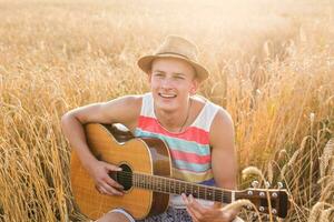 jovem homem jogando guitarra dentro a campo em pôr do sol foto