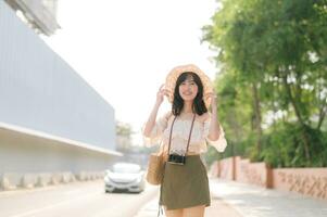 retrato do ásia jovem mulher viajante com tecelagem chapéu e cesta e uma Câmera em pé de a rua. viagem viagem estilo de vida, mundo viagem explorador ou Ásia verão turismo conceito. foto