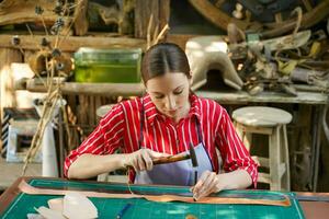 fechar-se jovem fêmea couro criador usando uma pequeno hummer com couro soco aço para faço uma couro cinto para clientes. foto
