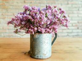 fechar-se lindo tolet flores dentro zinco vintage vaso em de madeira mesa e velho tijolo parede fundo. foto