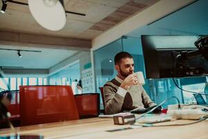 uma homem sentado às uma escrivaninha dentro a escritório bebendo café foto