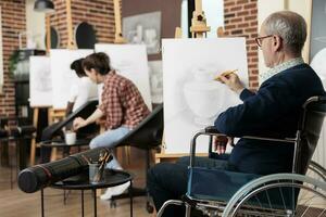 Senior homem com fisica deficiências sentado às cavalete durante grupo arte aula, cadeira de rodas do utilizador aumentando bem motor Habilidades através desenhando prática. Desativado pessoa noivando dentro criativo Atividades foto