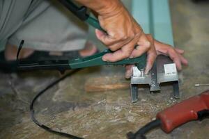 fechar-se mãos do construtor usando uma ilhó soco alumínio máquina trabalhando soco alumínio madeira serrada às construção local. foto