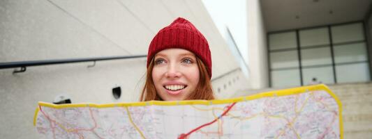 lindo menina turista senta em escadas com cidade mapa, planos dela jornada, parece para direção enquanto viajando por aí cidade, pesquisas rota para passeios turísticos foto