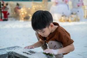 pequeno ásia Garoto jogando dentro artificial neve durante Natal festival foto