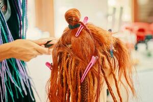 cabeleireiro tece tranças com vermelho kanekalon lindo ruiva garota. foto