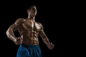 muscular e em forma jovem fisiculturista ginástica masculino modelo posando sobre Preto fundo. foto