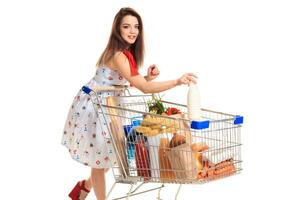 sorridente jovem mulher fazendo mercearia compras às a supermercado, ela é colocando uma leite garrafa dentro a carrinho foto