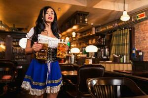 lindo fêmea garçonete vestindo tradicional dirndl e segurando enorme cervejas dentro uma bar. foto