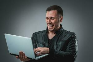 feliz homem segurando computador portátil em cinzento fundo foto