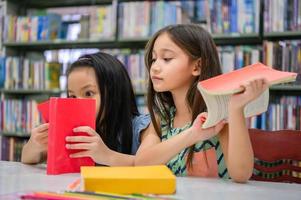 duas meninas bonitos amigos multiétnicos lendo livros juntos na biblioteca da escola. estilo de vida das pessoas e conceito de aprendizagem de educação. Feliz amizade crianças fazendo atividades de lazer para o teste de exame foto