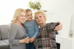 uma pequeno garota, mãe e avó com Smartphone às lar. foto