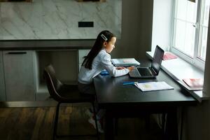 pequeno menina estudando conectados usando dela computador portátil às casa foto