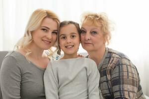 retrato do três gerações do mulheres Veja às Câmera posando para família foto, fofa pequeno menina abraço mãe e avó apreciar Tempo às lar, sorridente mãe, filha e avó gastar final de semana juntos foto