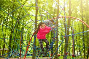 menina feliz em um parque de corda no fundo de madeira foto