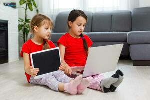 dois pequeno meninas estão jogando com computador portátil dentro sala de jogos às casa foto