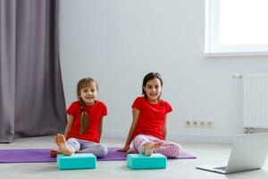 duas meninas praticando ioga, alongamento, fitness por vídeo no notebook. treinamento de educação on-line distante, aeróbico em casa. estilo de vida saudável, coronavírus, fique em casa. crianças esporte quarentena em casa. foto