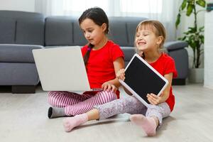 dois pequeno meninas estão jogando com computador portátil dentro sala de jogos às casa foto