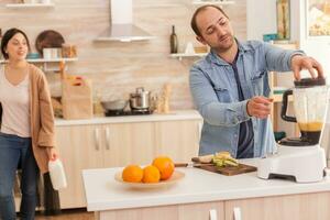 homem insípido vários frutas para delicioso batido e esposa é segurando leite garrafa dentro a fundo. saudável despreocupado e alegre estilo de vida, comendo dieta e preparando café da manhã dentro acolhedor ensolarado manhã foto