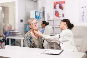 médico tocante Senior paciente pescoço para glândulas anormalidades dentro hospital escritório. médico examinando idosos mulher. foto
