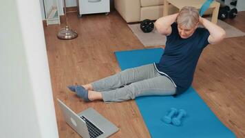 esportivo Senior mulher em ioga esteira exercício olhando às conectados ginástica programa. velho pessoa pensionista conectados Internet exercício Treinamento às casa esporte atividade às idosos aposentadoria era foto