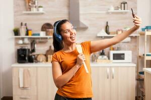 feliz mulher levando uma selfie dentro a manhã enquanto cantando usando colher. enérgico, positivo, feliz, engraçado e fofa dona de casa dançando sozinho dentro a casa. entretenimento e Leise sozinho às casa foto