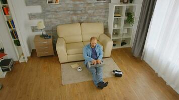 topo Visão do caucasiano homem trabalhando a partir de casa em uma computador portátil e bebericando café enquanto sentado em a chão foto