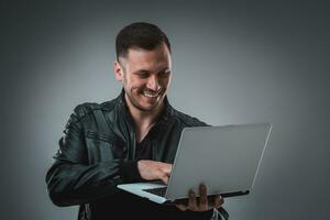 homem dentro Preto Jaqueta olhando às computador portátil, metade vez. segurando aberto computador portátil e trabalhando. emoção. foto