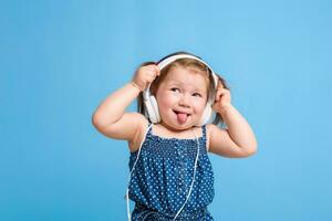 fofa pequeno menina dentro fones de ouvido ouvindo para música usando uma tábua e sorridente em azul fundo foto