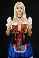 jovem sexy mulher vestindo uma dirndl com dois Cerveja canecas em Preto fundo foto