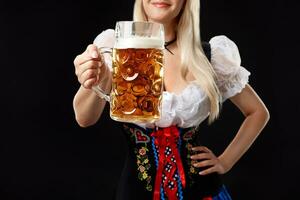 jovem sexy mulher vestindo uma dirndl com Cerveja caneca em Preto fundo. foto