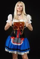 jovem sexy mulher vestindo uma dirndl com dois Cerveja canecas em Preto fundo. foto