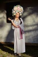 morena menina dentro uma branco ucraniano autêntico nacional traje e uma guirlanda do flores é posando contra uma branco cabana. foto