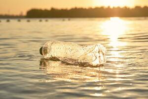 amassado plástico garrafa flutua em a superfície do a água. pôr do sol, verde árvores pessoas e ecologia. ribeirinha poluição. fechar-se tomada. foto