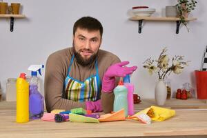 jovem bonito barbudo homem dentro a cozinha, mostra todos dele limpeza funcionários - detergentes, escovas, sprays. ele pensar ele é pronto para real limpeza foto