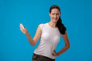 estúdio retrato do uma jovem lindo mulher dentro uma branco camiseta contra uma azul parede fundo. pessoas sincero emoções. foto