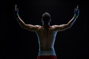 traseiro Visão do Forte jovem masculino boxer. ginástica masculino modelo vestindo boxe luvas em pé em Preto fundo. foto