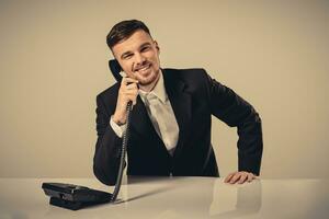 jovem homem dials a telefone número enquanto sentado dentro a escritório foto