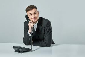 jovem homem dials a telefone número enquanto sentado dentro a escritório foto