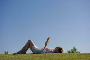 uma mulher deitado em a Relva lendo uma livro foto