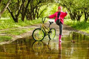 pequeno menina equitação bicicleta dentro água poça foto