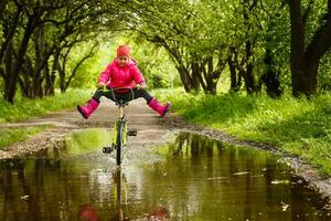 pequeno menina equitação bicicleta dentro água poça foto