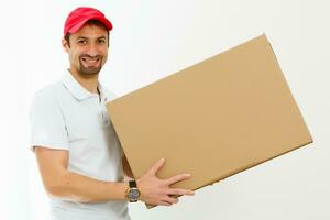 sorridente jovem Entrega homem segurando e carregando uma Caixa de papelão isolado em branco fundo foto