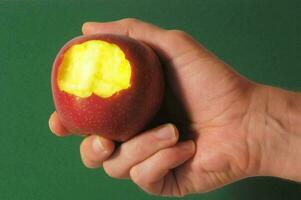 uma mão segurando a maçã com uma orifício dentro isto foto