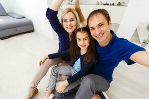 lindo jovem mãe, pai e seus filha estão fazer selfie usando uma telefone e sorridente enquanto sentado às casa foto