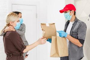 jovem mulher vestindo médico mascarar recebendo ordenado Comida a partir de a restaurante a partir de Entrega homem dentro de casa. prevenção do vírus espalhar foto