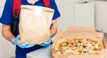 Entrega homem empregado dentro vermelho boné camiseta uniforme mascarar luvas dar Comida ordem pizza caixas isolado em amarelo fundo estúdio. serviço quarentena pandemia coronavírus vírus gripe 2019-ncov conceito foto